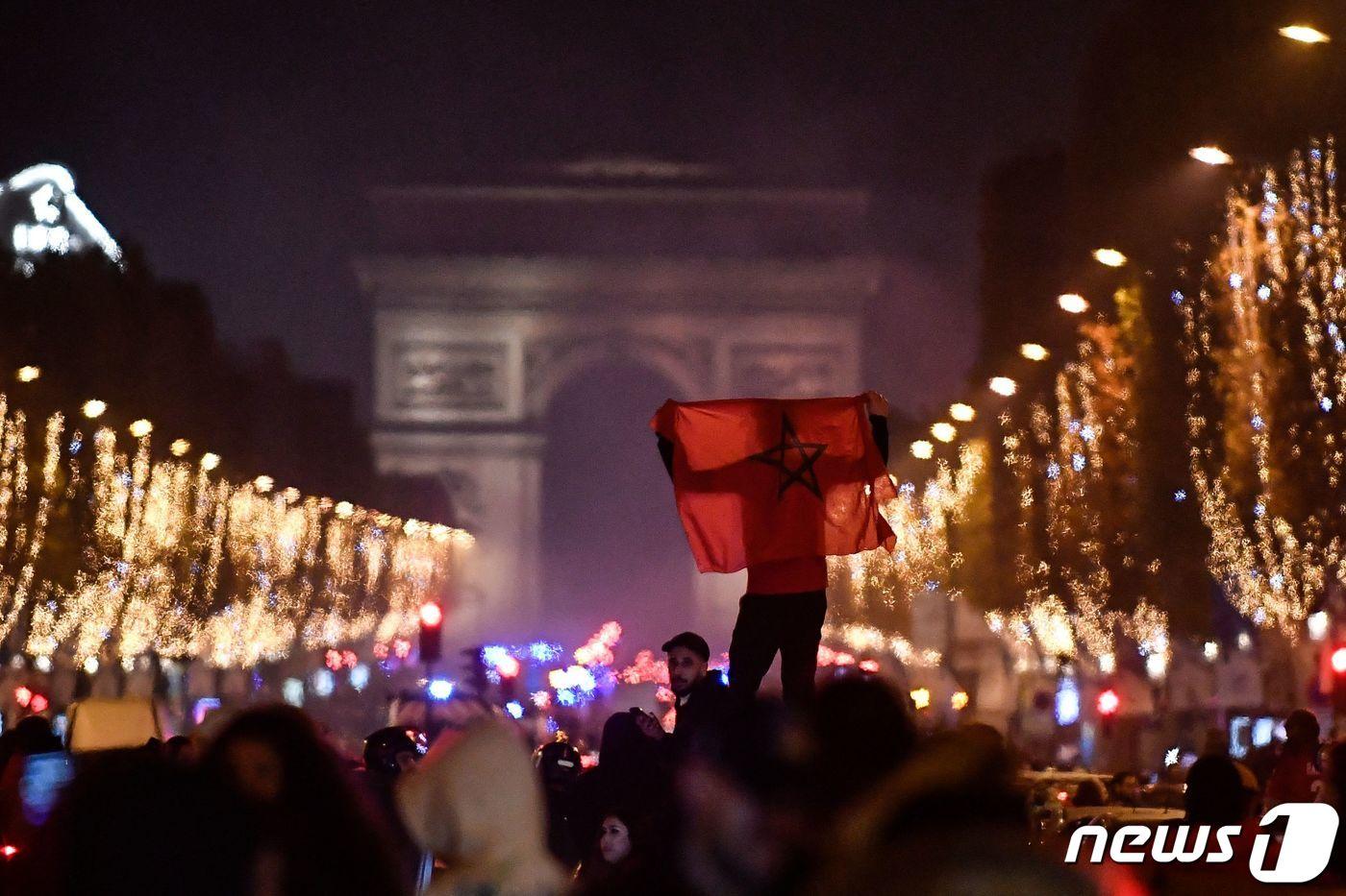 본문 이미지 - 6일(현지시간) 프랑스 파리 샹젤리제 거리에서 2022 카타르 월드컵 16강전 모로코대 스페인의 경기 후 모로코 축구 팬 한 명이 자국 대표팀 승리를 기뻐하며 모로코 국기를 두 손 높이 들고 있다. 이날 모로코는 승부차기 끝에 스페인을 상대로 극적인 승리를 거둬 월드컵 역사상 아랍권 최초로 8강에 진출한다. ⓒ AFP=뉴스1 ⓒ News1 김성식 기자