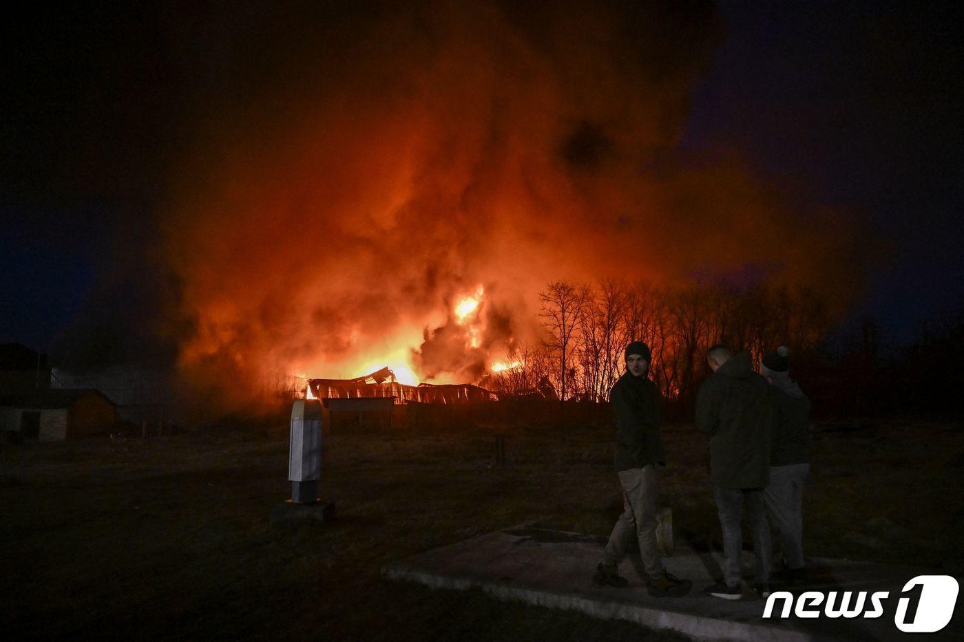 17일 키이우에서 러시아 군의 포격을 받아 불 타는 창고 앞에 우크라이나 군이 서 있다. ⓒ AFP=뉴스1 ⓒ News1 우동명 기자