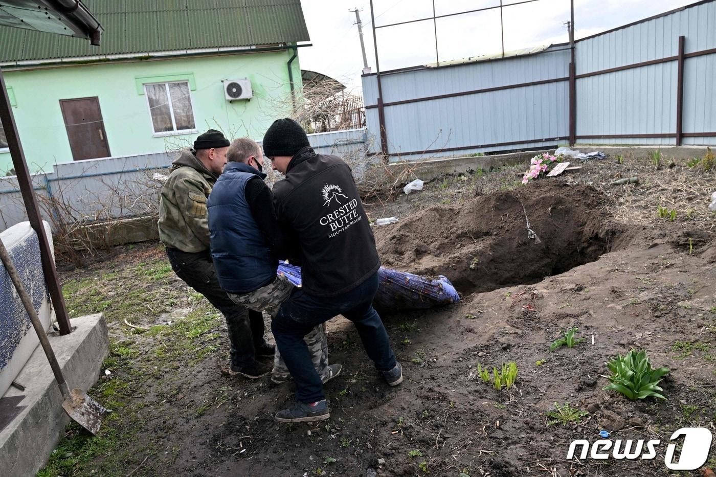 11일 (현지시간) 우크라이나 수도 키이우 인근 안드리우카의 주택 마당에서 주민들이 러시아 군의 집단 매장 민간인을 꺼내고 있다. ⓒ AFP=뉴스1 ⓒ News1