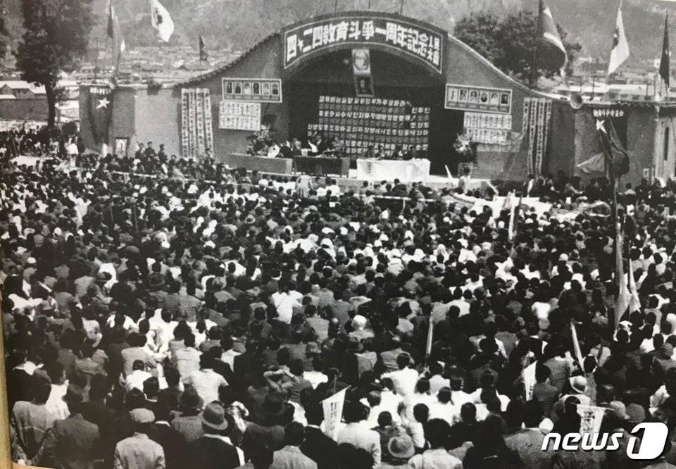 본문 이미지 - '4·24교육투쟁' 1주년 기념 중앙인민대회(1949년 4월25일·일본 고베시 미나토가와 공원)에 4만5000명의 군중이 참가했다. 무대엔 투옥 중인 동포 사진이 걸려 있다. (출처=잡지 '이어') ⓒ News1