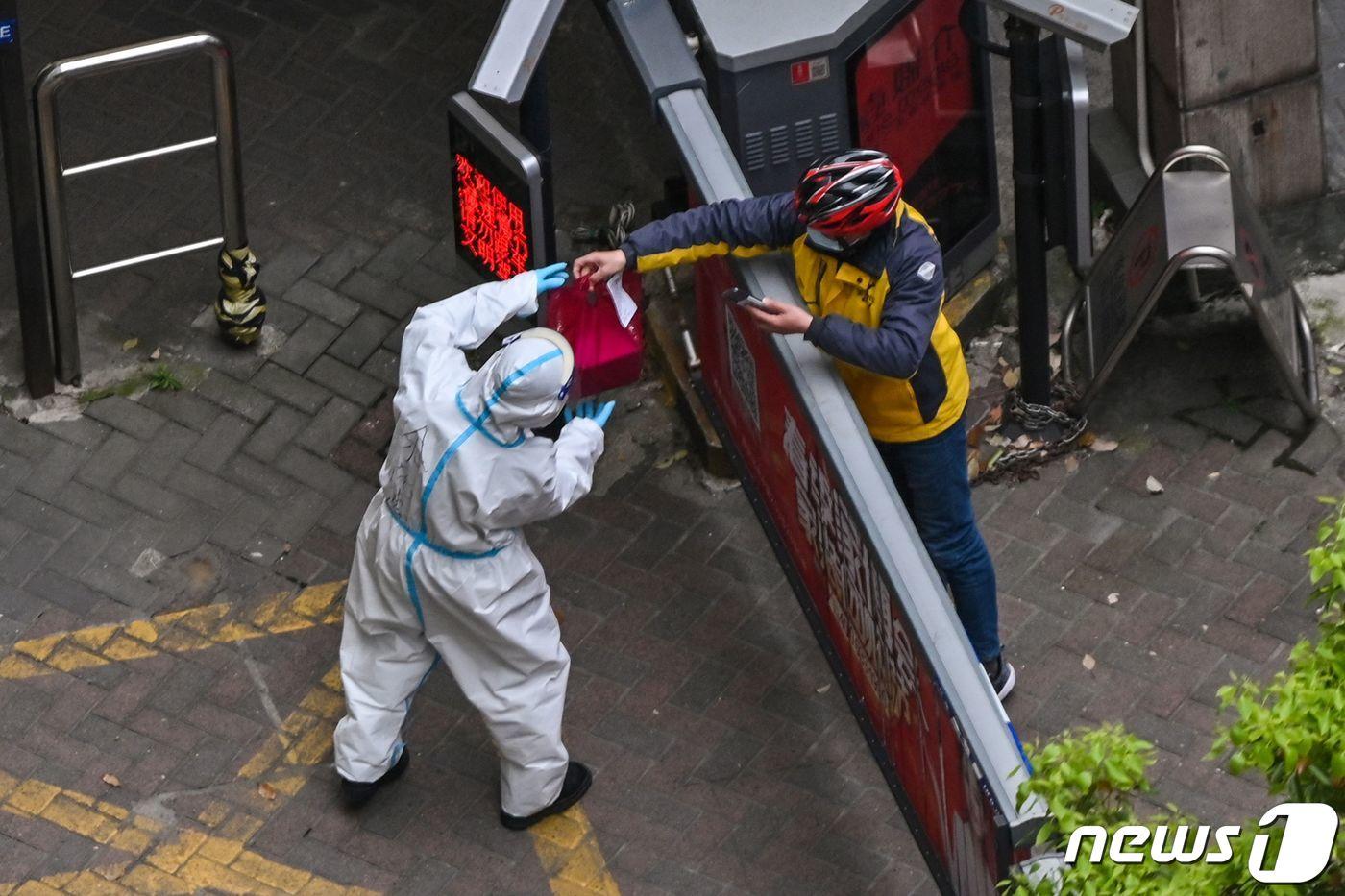 5일 (현지시간) 코로나19 봉쇄 조치가 연장된 중국 상하이에서 방호복을 입은 사람이 배달원으로부터 격리 주민들에게 전달할 물건을 대신 받고 있다. ⓒ AFP=뉴스1 ⓒ News1 우동명 기자