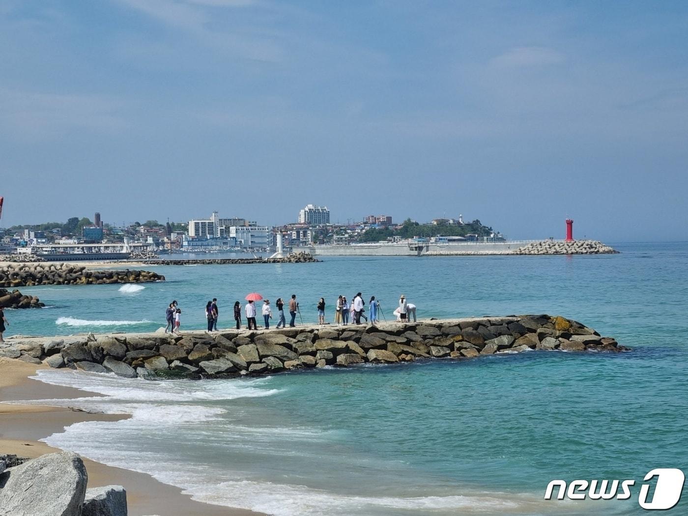 본문 이미지 - '도깨비' 촬영지로 유명한 강원 강릉 영진해변 '도깨비 방사제'에 기념사진을 찍으려는 연인 관광객들이 줄지어 차례를 기다리고 있다. 방사제 뒤로 보이는 빨간 등대는 넷플릭스 오리지널 시리즈 '더글로리' 촬영지인 소돌항 등대다. (뉴스1 DB)
