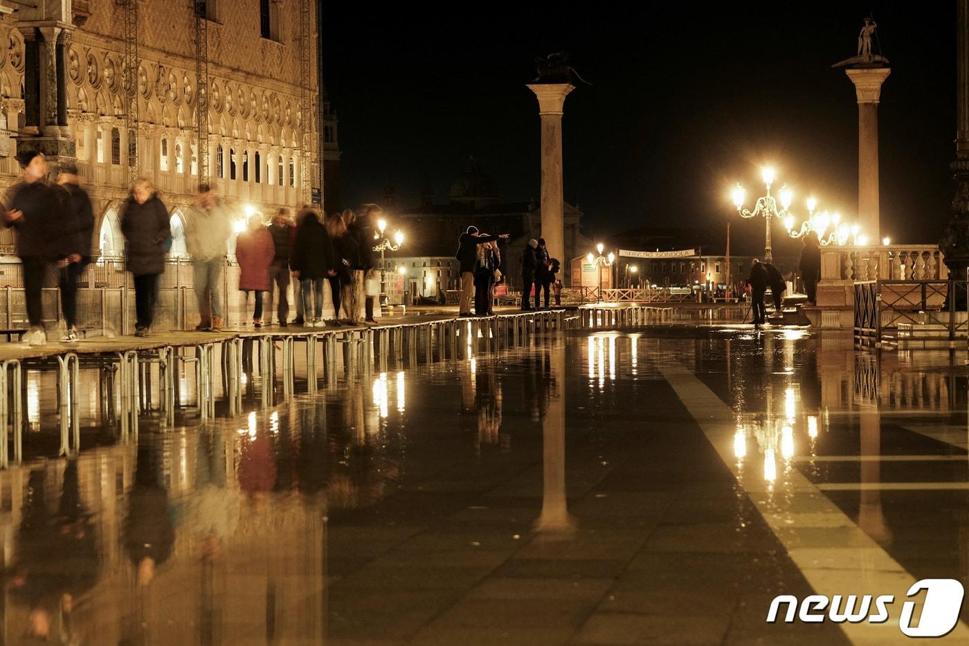본문 이미지 - 17일(현지시간) 이탈리아 베네치아에서 사람들이 물에 잠긴 산마르코 광장을 건너고 있다. 베네치아에서는 매년 9~이듬해 4월 사이 조수가 상승해 범람하는 '아쿠아 알타' 현상이 나타난다. 보행자를 위해 수면 위로 통로가 설치됐다. 2023.01.17/ ⓒ 로이터=뉴스1 ⓒ News1 권진영 기자