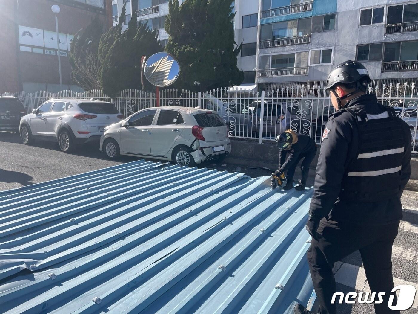 본문 이미지 - 지난 24일 오후 2시49분쯤 양산시 삼호동의 한 건물의 패널 지붕이 바람에 날아가 도로에 주차돼 있던 차량을 덮쳐 소방당국이 안전조치를 하고 있다.(경남소방본부 제공)
