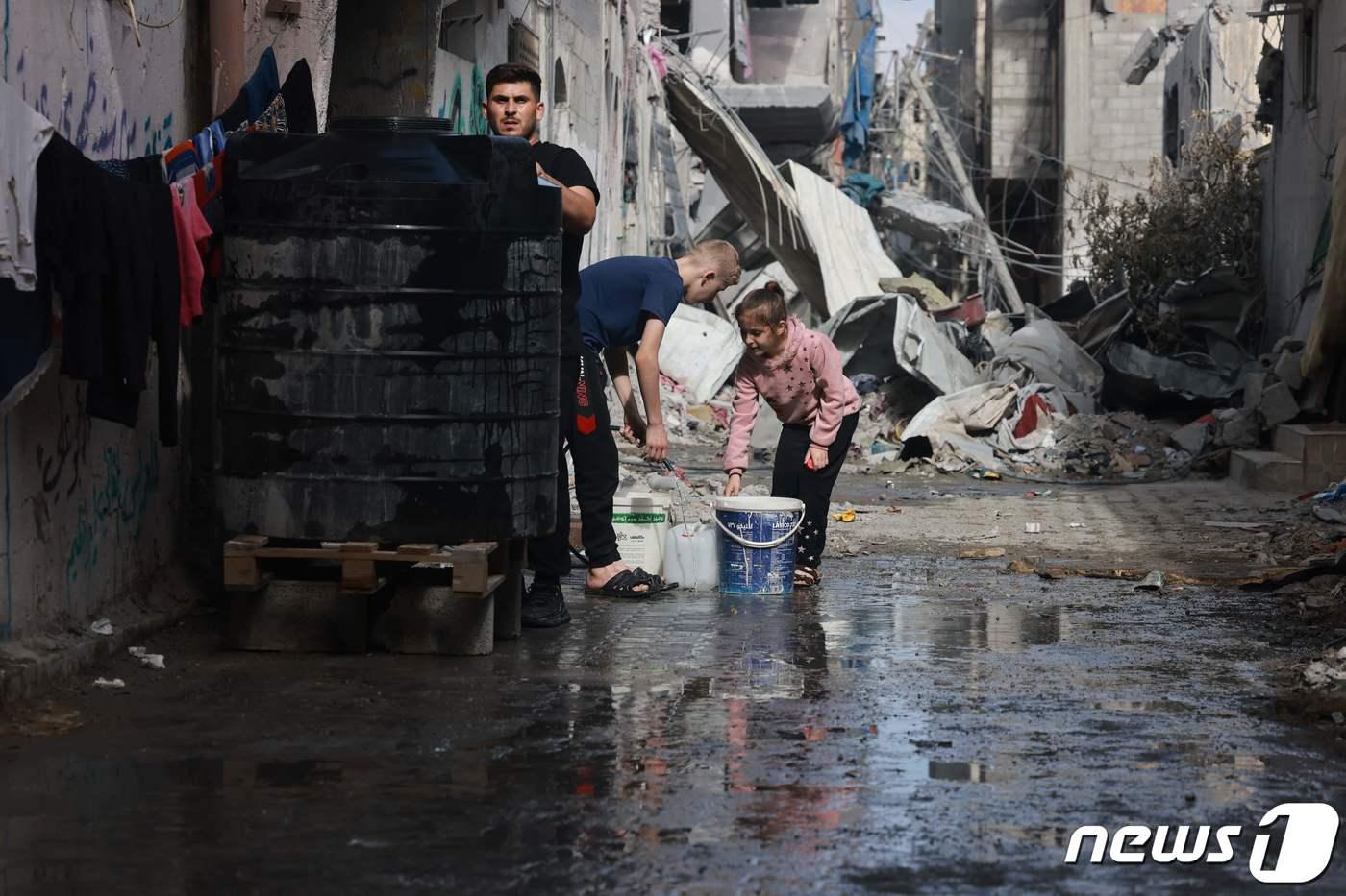 본문 이미지 - 14일(현지시간) 폭우가 내린 가자지구 부레이지 난민촌에서 팔레스타인 어린이들이 거리에 고인 물을 퍼내고 있다. 23.11.14 ⓒ AFP=뉴스1 ⓒ News1 김예슬 기자