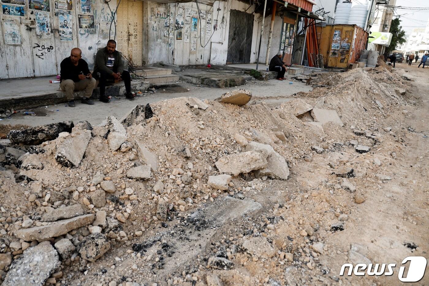 본문 이미지 - 26일(현지시간) 이스라엘이 점령한 요르단강 서안지구 제닌에서 팔레스타인인들이 무너진 길가 한 켠에 앉아있다. 2023.11.27 ⓒ 로이터=뉴스1 ⓒ News1 정지윤 기자