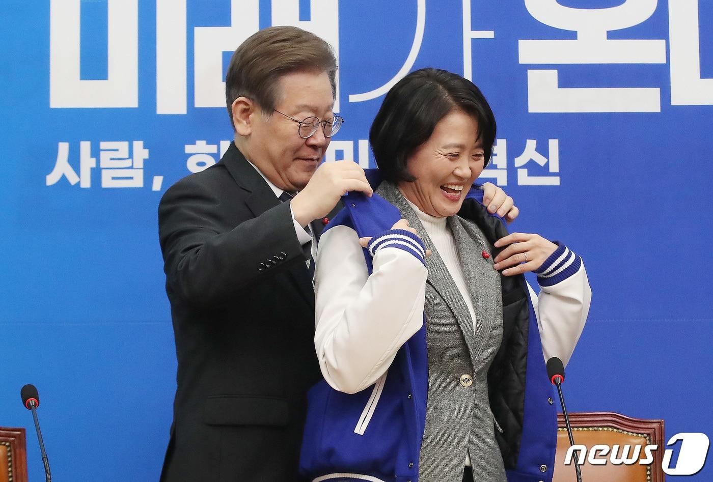 이재명 더불어민주당 대표가 11일 오전 서울 여의도 국회에서 열린 더불어민주당 1호 인재영입식에서 인재영입 1호 인사인 박지혜 변호사에게 민주당 점퍼를 입혀주고 있다. 더불어민주당 인재 영입 1호 인사인 박지혜 변호사는 환경단체에서 기후변화 관련 활동을 펼쳐온 여성 법률가다. 2023.12.11/뉴스1 ⓒ News1 임세영 기자