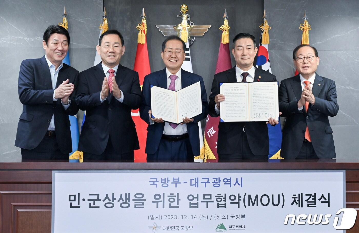 홍준표 대구시장(가운데)과 신원식 국방부 장관이 지난해 12월14일 국방부에서 열린 민·군 상생을 위한 업무협약 체결식에서 협약서에 서명한 뒤 지역 국회의원들과 함께 기념촬영을 하고 있다. (대구시 제공) 2023.12.14/뉴스1 ⓒ News1 공정식 기자