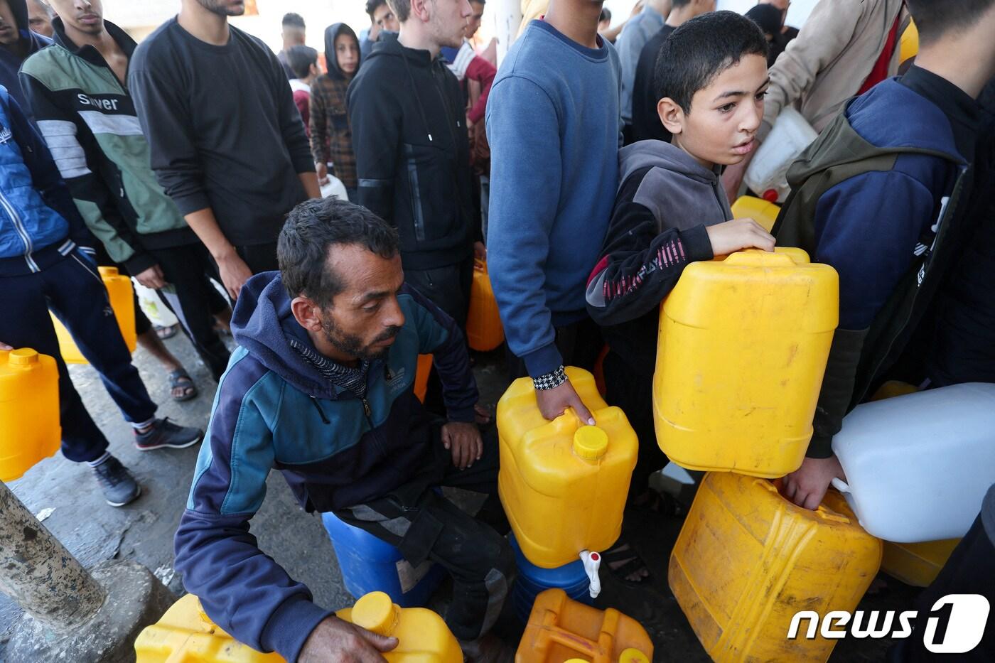 본문 이미지 - 4일(현지시간) 가자지구 남부 칸유니스 지역에서 팔레스타인인들이 물을 담기 위한 통을 들고 줄지어 서고 있다. 2023.12.04 ⓒ 로이터=뉴스1 ⓒ News1 정지윤 기자