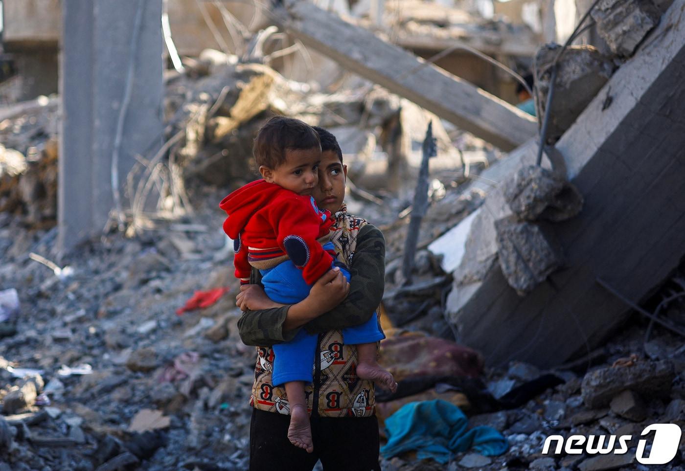 본문 이미지 - 한 팔레스타인 소년이 4일(현지시간) 가자지구 남부 라파 지역에서 아이를 들고 걱정스러운 눈빛으로 무너진 건물들을 바라보고 있다. 2023.12.04 ⓒ 로이터=뉴스1 ⓒ News1 정지윤 기자