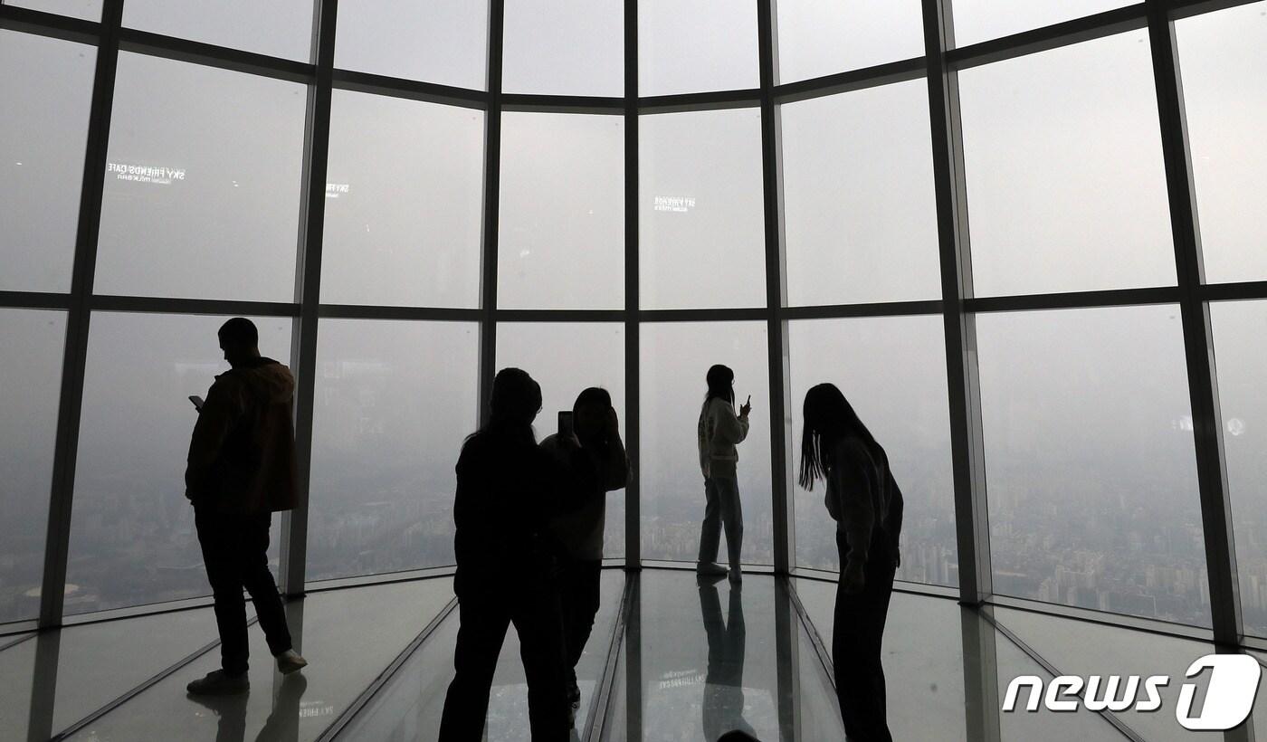 본문 이미지 - 서울 미세먼지 농도가 ‘나쁨’을 보이고 있는 6일 오후 서울 송파구 롯데월드타워 서울스카이를 찾은 시민들이 미세먼지와 흐린 날씨로 뿌옇게 보이는 서울도심을 바라보고 있다. 2023.12.6/뉴스1 ⓒ News1 박세연 기자