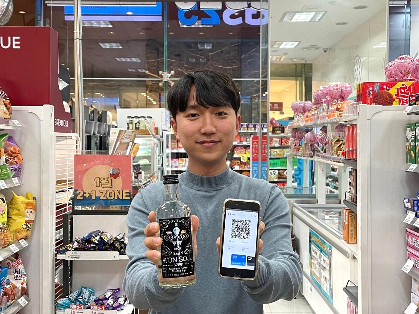 본문 이미지 - 모델이 원소주 스피릿과 GS페이 화면이 보이는 휴대폰을 들고 있는 모습(GS리테일 제공).