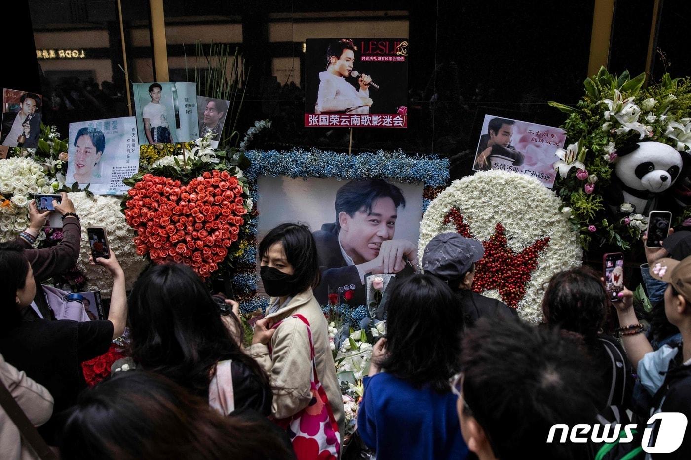 본문 이미지 - 홍콩의 가수 겸 배우였던 장국영의 사망 20주기를 맞은 1일(현지시간) 홍콩에서 시민들이 길가에 놓인 추모 화환과 그의 생전 모습을 카메라에 담고 있다. 2023.04.01. ⓒ AFP=뉴스1 ⓒ News1 김성식 기자