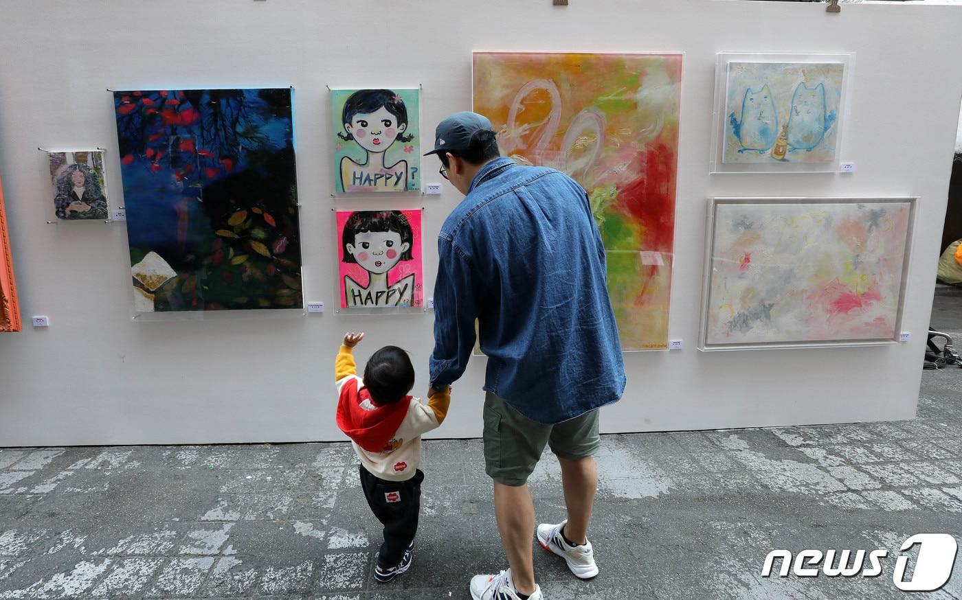 서울 용산구 이태원 세계음식문화거리에서 열린 거리전시회 '헤이, 이태원'을 찾은 시민들이 전시된 작품을 살펴보고 있다. 이번 전시는 이태원의 새로운 성장과 도약, 상권 활성화를 위해 '헤이, 이태원 프로젝트'의 일환으로 대한민국인플루언서협회와 이태원관광특구연합회가 함께 기획했다. ⓒ News1 박세연 기자