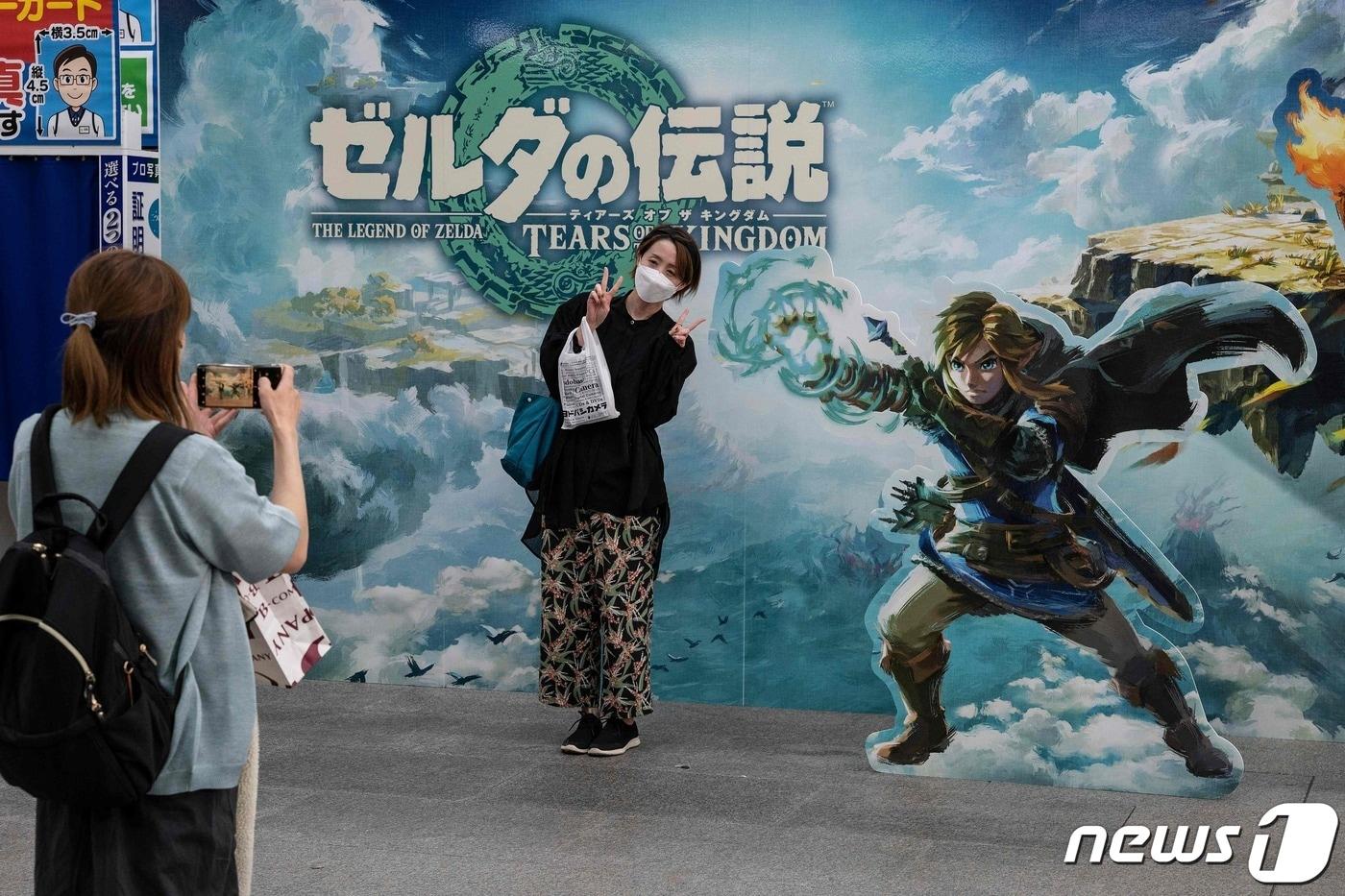 지난 5월12일 일본 도쿄에서 닌텐도의 인기 게임 ''젤다의 전설 :티어스 오브 더 킹덤'을 구입한 여성이 광고벽 앞에서 기념 사진을 찍고 있다. ⓒ AFP=뉴스1 ⓒ News1 권진영 기자
