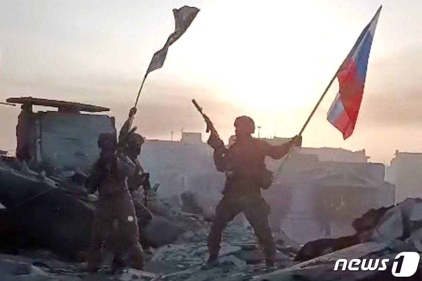 본문 이미지 - 20일(현지시간) 우크라이나 바흐무트의 파괴된 건물 지붕에서 러시아 용병 기업 바그너 그룹의 병사들이 국기와 깃발을 흔들며 점령을 환호하고 있다. ⓒ AFP=뉴스1 ⓒ News1 우동명 기자