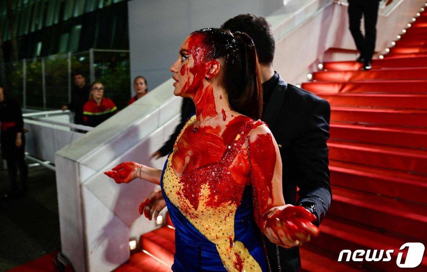 본문 이미지 - 한 여성이 프랑스 남부 칸 팔레 데 페스티벌 레드카펫에서 자신의 몸에 붉은 책 액체를 부었다. ⓒ AFP=뉴스1