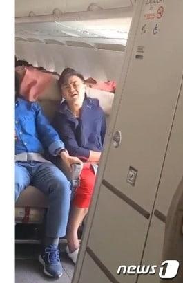 본문 이미지 -  26일 낮 제주발 대구행 아시아나 항공기가 대구공항 상공에서 착륙 준비를 하던 중 창문쪽에 앉아있던 이모(33·)씨가 갑자기 비상구 문을 여는 바람에 강한 바람이 기내로 들어왔다. 이씨 바로옆에 앉아 바람을 직접 맞아 힘들어하는 모습의 빨간바지 차림의 이윤준씨는 착륙과정에서 범인이 비행기 밖으로 뛰어내려는 것을 붙잡아 또다른 불상사를 맞았다. (유튜브 갈무리) ⓒ 뉴스1