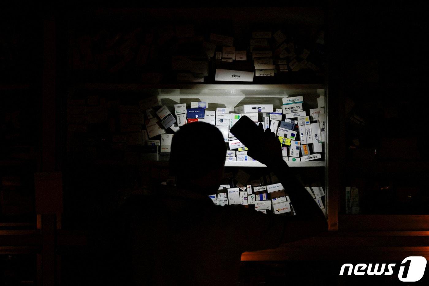 지난해 10월4일(현지시간) 대규모 블랙아웃으로 전력이 끊기자, 방글라데시 다카의 한 약국에서 약사가 핸드폰 불빛으로 약을 찾는 모습. 22.10.04 ⓒ 로이터=뉴스1 ⓒ News1 김예슬 기자