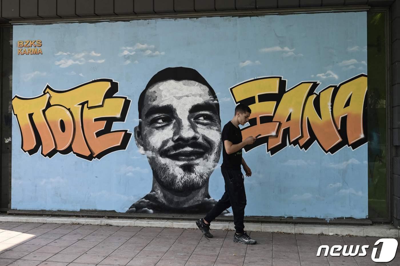 지난해 2월 그리스 북부서 경쟁 관계인 축구 클럽의 팬을 공격해 숨지게 한 혐의로 재판에 넘겨진 상대 클럽의 팬 7명이 12일(현지시간) 종신형을 선고받은 가운데 한 남성이 그리스 테살로니키의 한 골목에 그려진 희생자 알키스 캄파노스를 추모하는 벽화 앞을 지나가고 있다. 2023.07.12/ ⓒ AFP=뉴스1 ⓒ News1 박재하 기자