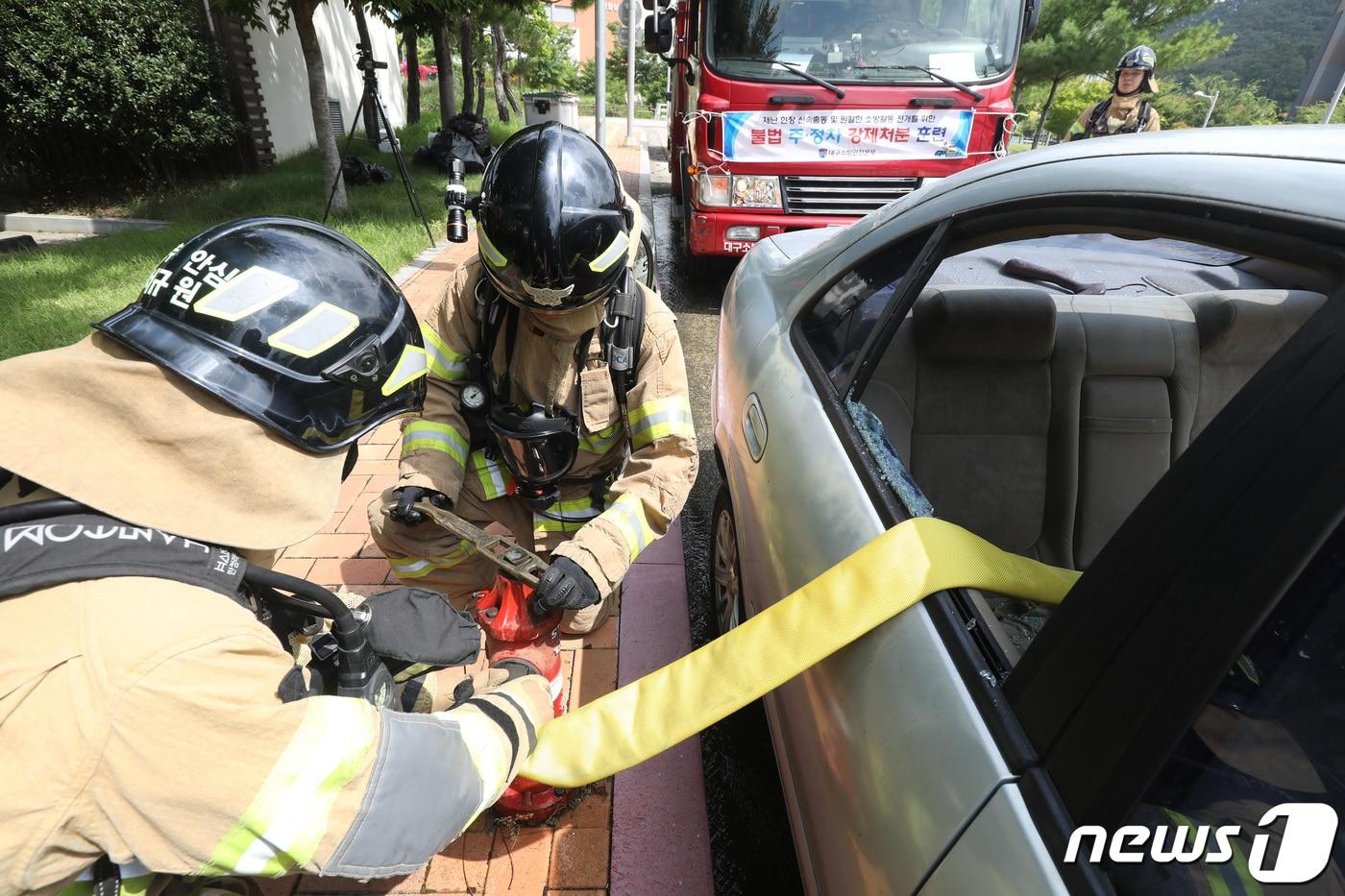 본문 이미지 - 8월14일 대구 동구 동내동 일대에서 열린 재난현장 신속출동과 원활한 소방활동 전개를 위한 '불법 주·정차 강제처분 훈련'에서 소방관이 적색 노면표시가 설치된 소화전 주변 5m 이내 주차 차량의 유리창을 깨트린 뒤 소방호스를 연결하고 있다. 2023.8.14/뉴스1 ⓒ News1 공정식 기자