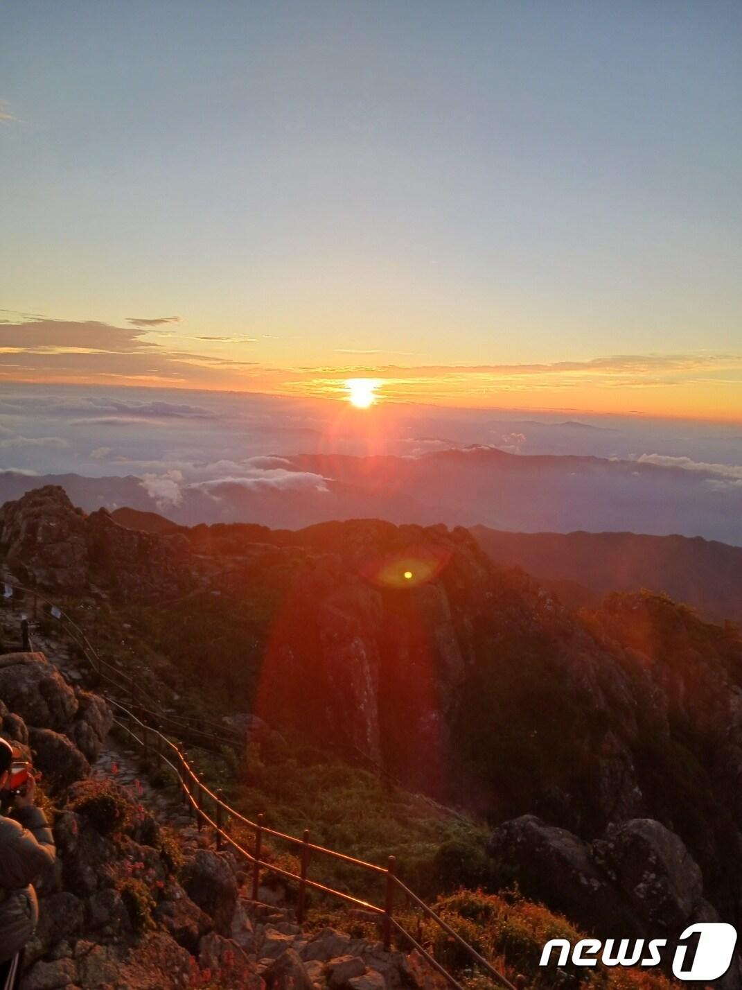본문 이미지 - 구름과 안개를 헤치고 천왕봉의 해가 떠오르고 있다.  주변을 붉게 물들이며 여명을 밝힌다. 아름답고 웅장하다. 역광이라  찍기가 쉽지 않아 동행한 산우(山友)에게 사진을 얻었다. 앞에 흰 점 모양은 다른 등반객이 일출 장면을 찍기 위해 띄운 드론이다. ⓒ 뉴스1