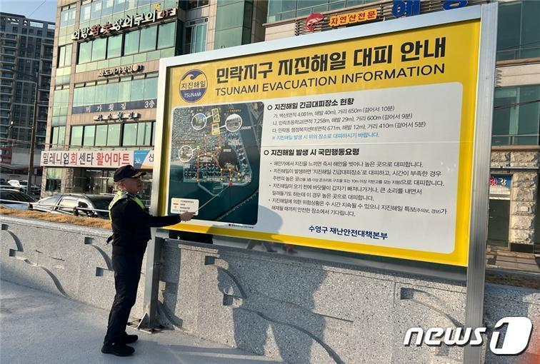 본문 이미지 - 광안리파출소 직원이 수영구 지진해일 대피 안내판을 점검하고 있다. (부산해경 제공)