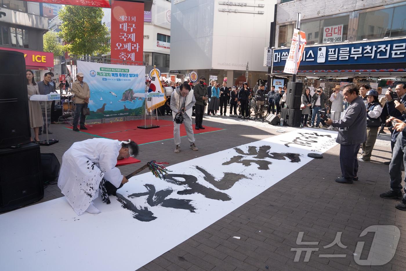 본문 이미지 - 24일 서예가 이홍재 씨가 붓을 들어 대형 천막에 "돌아오라, 독도강치여!"라는 내용을 쓰고 있다.(독도시민연대 제공)