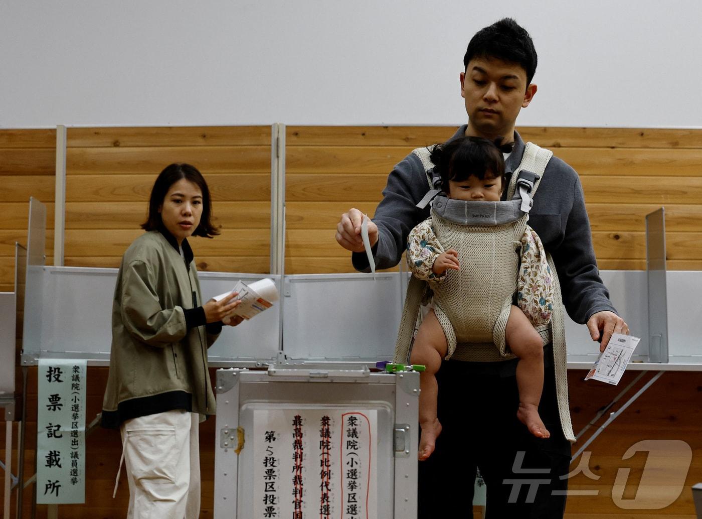 본문 이미지 -  일본 도쿄의 한 투표소에서 한 남성이 아기띠를 메고 제50회 중의원 선거 투표에 참여하고 있다. 2024.10.27/ ⓒ 로이터=뉴스1 ⓒ News1 권진영 기자