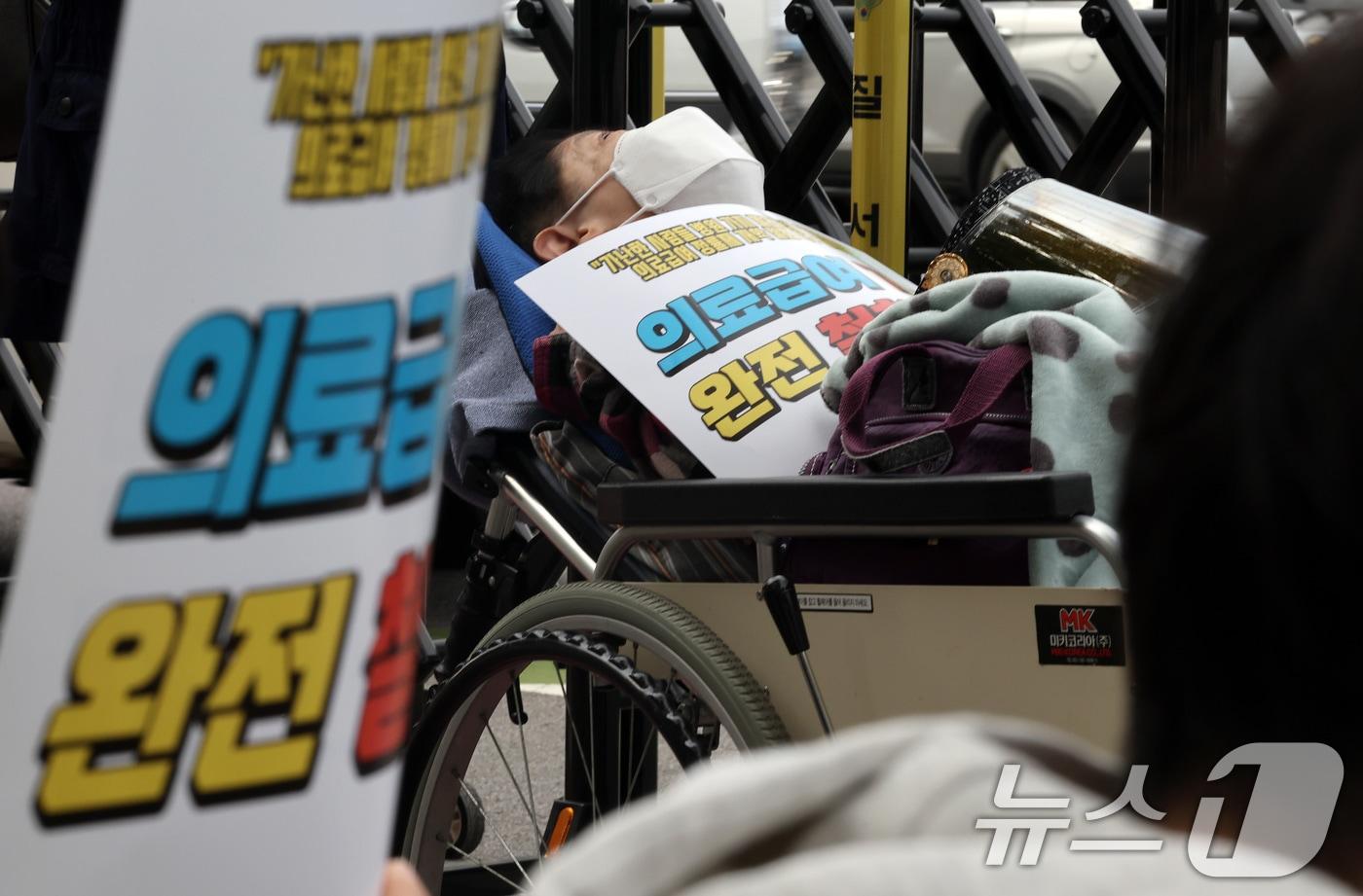 29일 오후 서울 종로구 정부서울청사 인근에서 참여연대와 빈곤사회연대 등 시민단체 주최로 열린 의료급여 정률제 개악 철회 촉구 결의대회에 한 집회 참석자가 휠체어에 누워 있다. 2024.10.29/뉴스1 ⓒ News1 이동해 기자