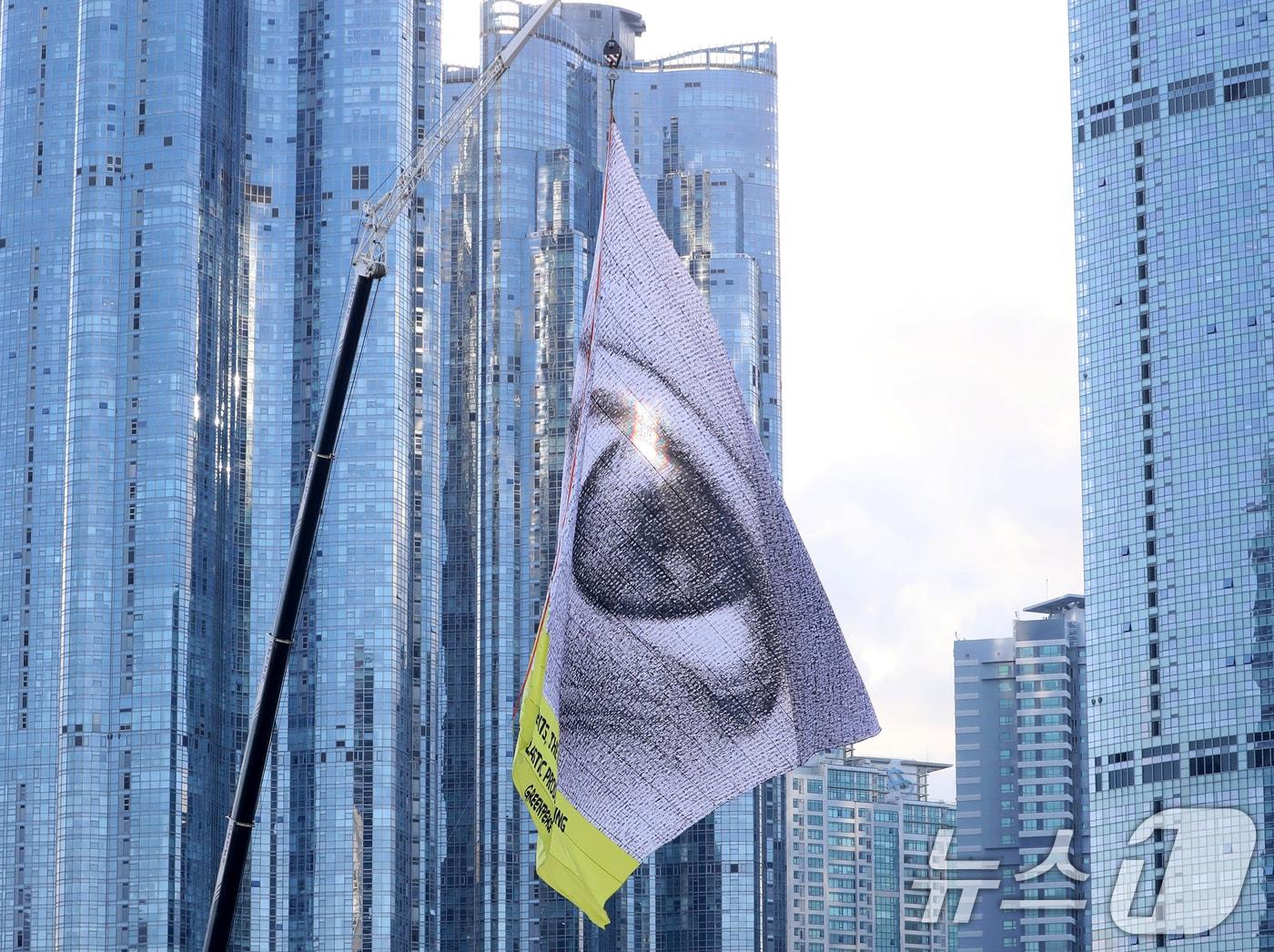 본문 이미지 - 국제 환경보호 단체인 그린피스가 부산 해운대구 수영만요트경기장 내 건물 10층 높이의 크레인에 가로 30m, 세로 24m 크기의 초대형 눈 형상 깃발을 설치해 퍼포먼스를 벌이고 있다. 플라스틱 협약을 &#39;전 세계가 지켜보고 있다&#39;&#40;WeAreWatching&#41;는 메시지다. 2024.11.25/뉴스1 ⓒ News1 윤일지 기자