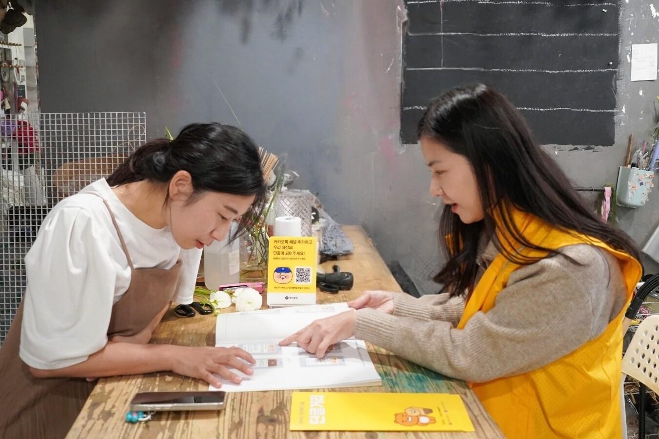 본문 이미지 - 인천 부평구 문화의거리에서 강미소 '메리꽃방' 사장(왼쪽)이 카카오 디지털 튜터의 교육을 받고 있다. (카카오 제공)