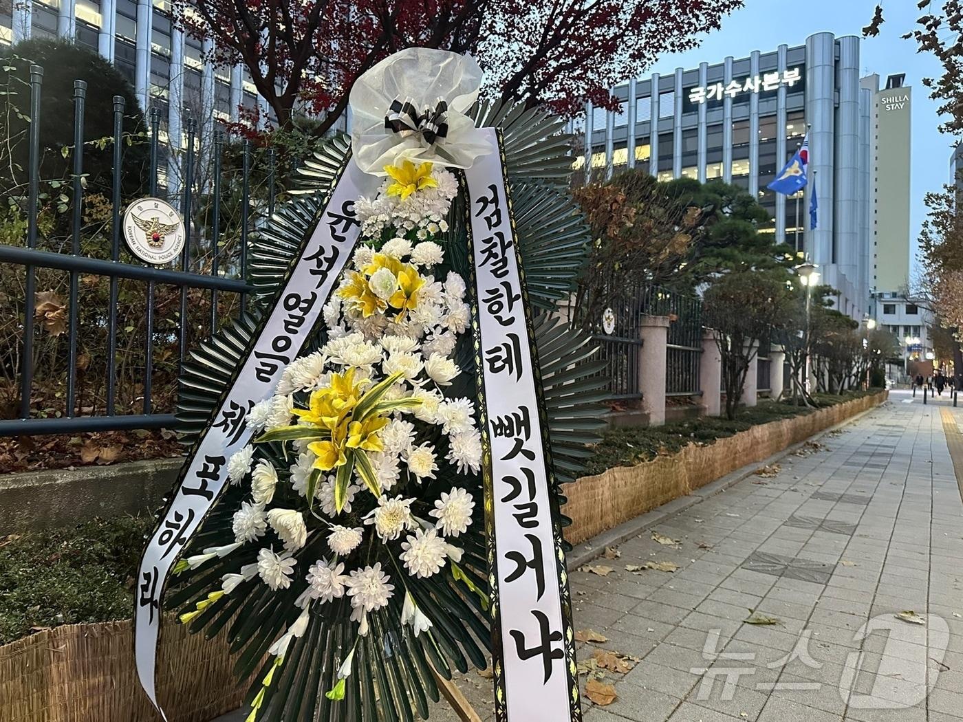 본문 이미지 - 12일 오후 서울 서대문구 미근동 경찰청사 정문 인근 울타리에는 "윤석열을 체포하라, 검찰한테 뺏길거냐" 내용이 담긴 근조화환이 설치됐다.