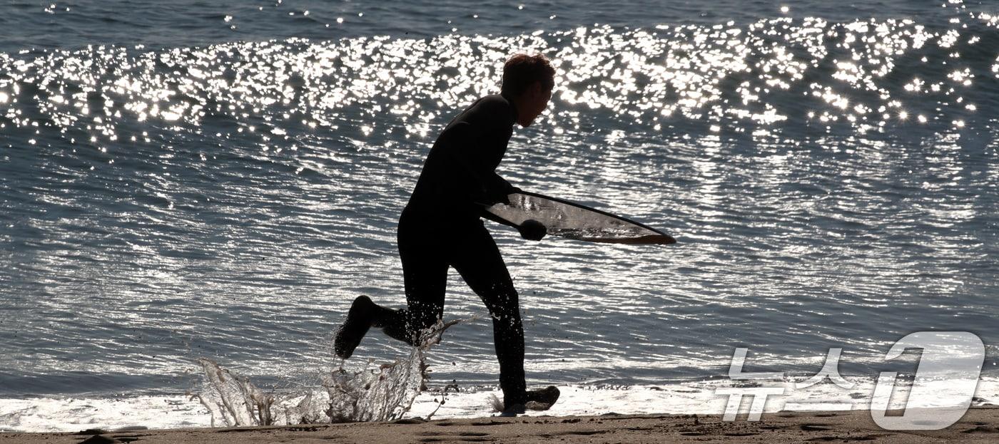 부산 해운대구 송정해수욕장에서 서퍼가 윤슬이 비치는 겨울 바다로 뛰어들며 서핑을 즐기고 있다. 2024.12.18/뉴스1 ⓒ News1 윤일지 기자