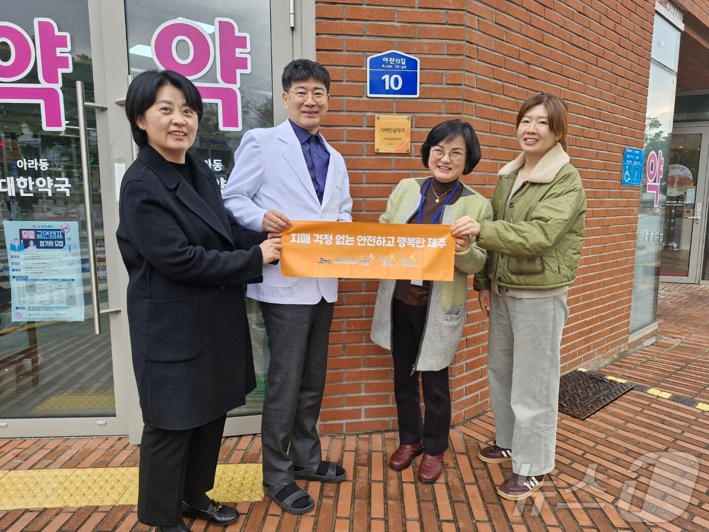 본문 이미지 - 제주 치매안심약국이 100곳으로 확대됐다. 치매안심약국과 제주도 관계자가 슬로건을 들고기념촬영을 하고 있다.(제주도 제공)