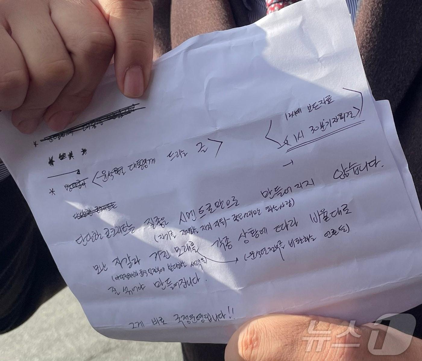 본문 이미지 - 공천 거래 혐의로 구속기소된 명태균 씨 측 변호인이 5일 경남 창원시 창원지방검찰청 앞에서 기자회견을 열고 명 씨가 전달한 '윤 대통령에게 드리는 글'이라는 제목의 옥중 메시지를 대독했다. 사진은 명 씨 변호인이 명 씨로부터 듣고 받아 적어온 메시지 내용을 적은 종이를 들고 있는 모습.2024.12.5/뉴스1 강정태 기자