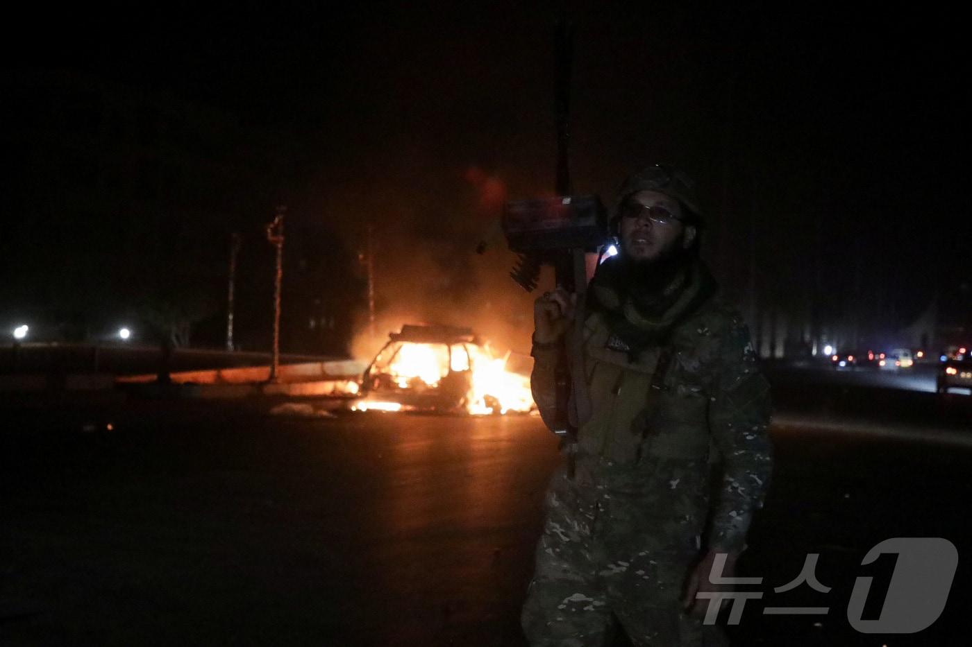 2024년 12월 5일 시리아 하마에서 시리아 반군이 시리아 북부를 가로질러 진격하는 동안 하마시를 점령한 후 반군 전사가 불이 붙은 차량 근처에서 무기를 들고 있다. REUTERS/Mahmoud Hassano ⓒ 로이터=뉴스1 ⓒ News1 박은정 기자