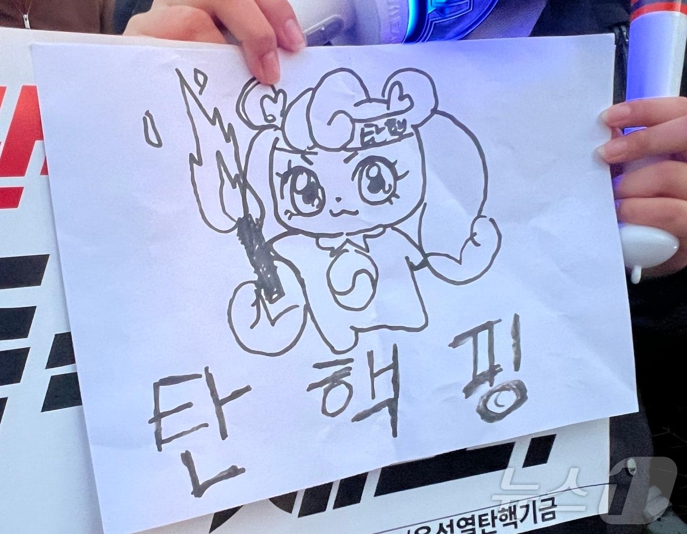 본문 이미지 - 8일 오후 서울 여의도 국회의사당역 인근에서 촛불행동의 주최로 열린 촛불문화제에 한 시민이 캐릭터 '하츄핑'을 패러디한 그림을 들고 참가하고 있다. 2024.12.08/뉴스1 ⓒ News1 김민수 기자