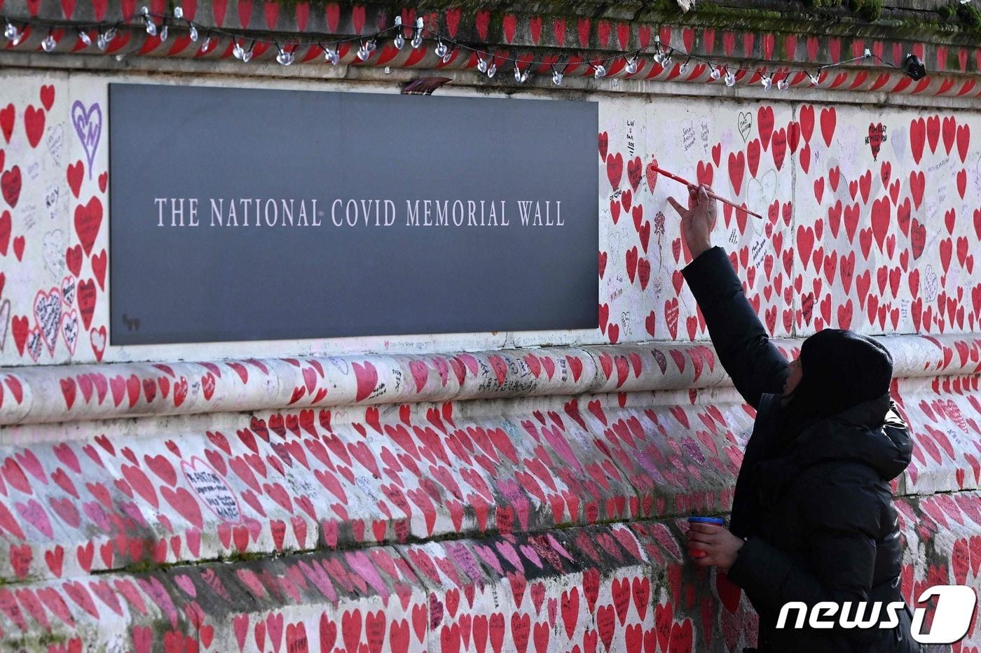 3일(현지시간) 코로나19로 목숨을 잃은 사람들을 기리는 영국 런던의 국립 코로나 기념 벽에 한 사람이 하트 모양을 그리고 있다. 2024.03.03 ⓒ AFP=뉴스1 ⓒ News1 정지윤 기자
