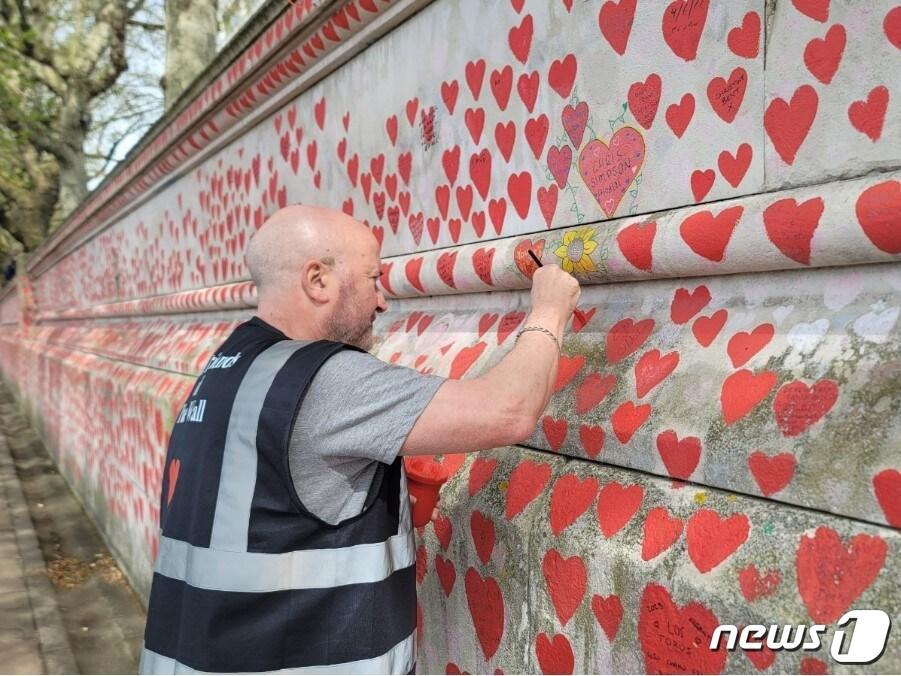 본문 이미지 - 12일&#40;현지시간&#41; 오후 국립 코로나19 추모의 벽에 하트를 덧칠하는 자원봉사자 테리 샌드웰&#40;68&#41;. 그는 지난 2020년 12월 코로나19 감염병으로 인해 사랑하는 아내와 사별해야 했다. @ 조아현