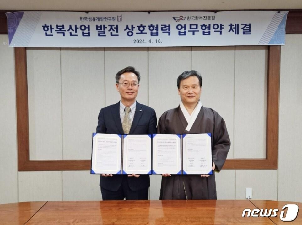 본문 이미지 - 호요승 한국섬유개발연구원장(왼쪽)과 박후근 한국한복진흥원장이 한복산업분야 상호 협력과 발전을 위한 업무협약을 체결한 뒤 협약서를 펼쳐 보이고 있다.(섬유개발연구원 제공)