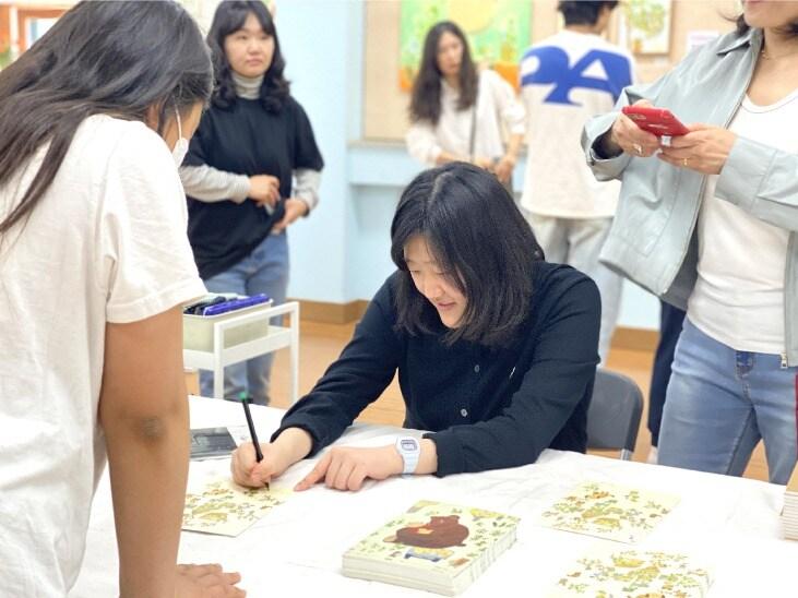 본문 이미지 - 경기 양평군 조현초에서 열리는 윤다냐 초대전에서 윤다냐 작가가 사인을 해주는 모습. 시스플래닛 제공.