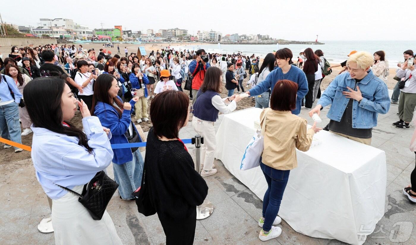 12일 제주시 이호테우해수욕장에서 슈퍼주니어-D&E가 일본인 관광객들에게 '슈퍼주니어-D&E와 함께 가는 SDGs 투어(지속가능한 여행) in 제주' 기념품을 전달하고 있다.(제주관광공사 제공)