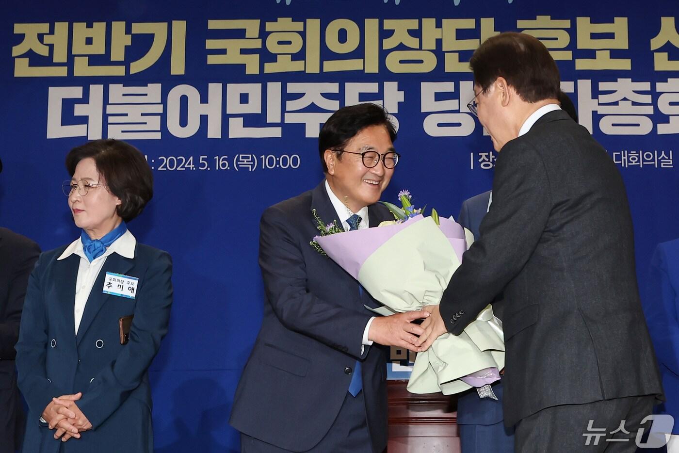 본문 이미지 - 더불어민주당 국회의장 후보에 당선된 우원식 의원이 16일 서울 여의도 국회 의원회관에서 열린 제22대 국회 전반기 국회의장단 후보 선출을 위한 더불어민주당 당선자총회에서 이재명 대표에게 꽃다발을 받고 있다. 왼쪽은 추미애 후보. 2024.5.16/뉴스1 ⓒ News1 김민지 기자