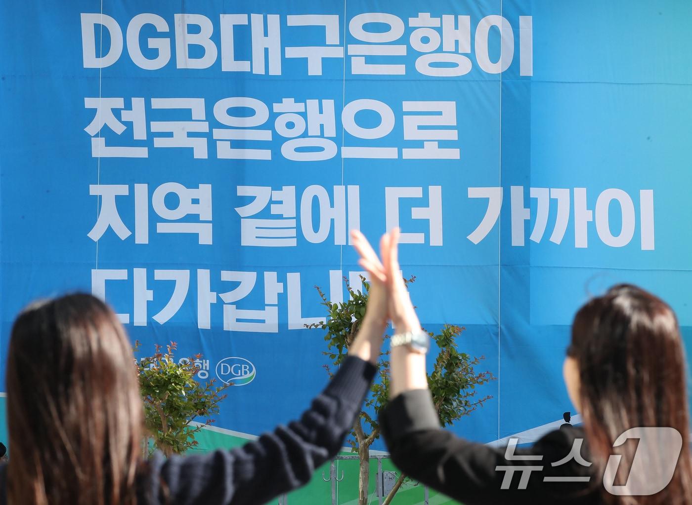 본문 이미지 - 16일 오후 대구 수성구 대구은행 본점 앞 열린광장에서 은행 직원들이 '대구은행의 시중은행 전환 인가'를 축하하는 현수막 앞에서 하이파이브를 나누고 있다. 2024.5.16/뉴스1 ⓒ News1 공정식 기자