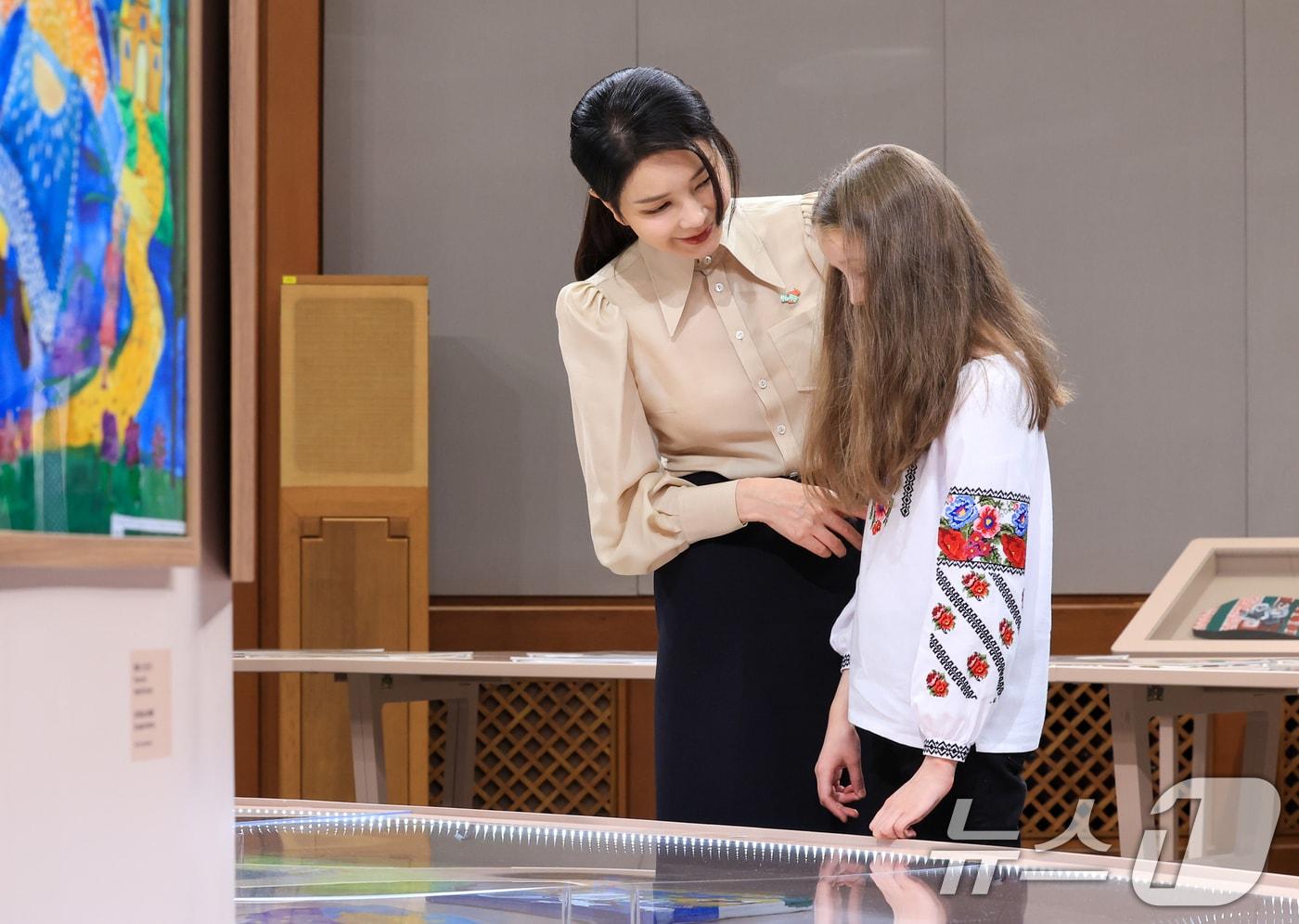 본문 이미지 - 윤석열 대통령 부인 김건희 여사가 21일 청와대 춘추관에서 열린 '희망을 그리는 아이들: 우크라이나 아동 그림전'을 찾아 우크라이나 어린이와 함께 지뢰탐지견(patron)에 대한 이야기를 나누며 14살 우크라이나 아동인 다리아 포포바가 지뢰탐지견을 그린 '우리 각각은 영웅이다' 작품을 감상하고 있다. (대통령실 제공) 2024.5.21/뉴스1 ⓒ News1 오대일 기자