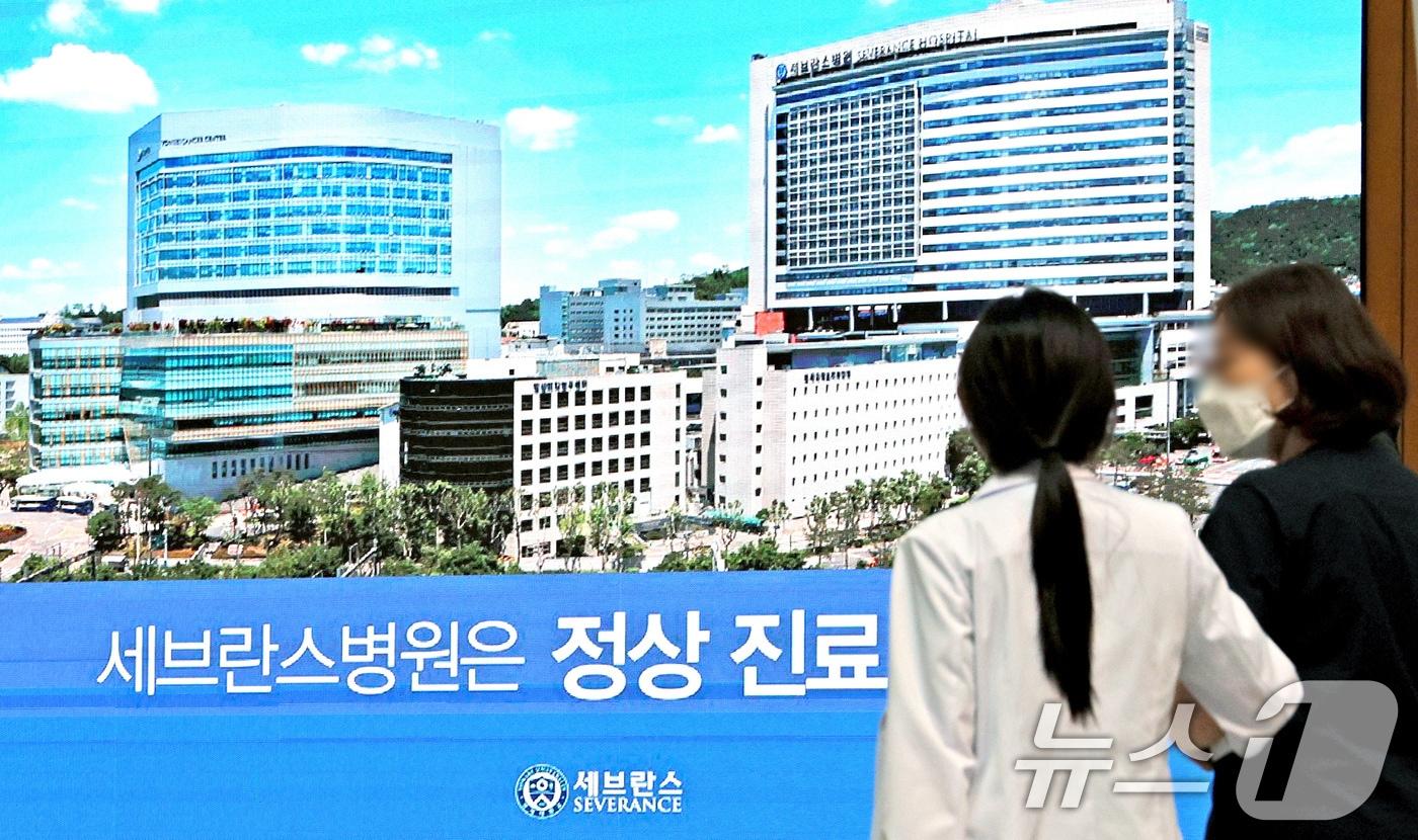 본문 이미지 - 연세 세브란스 교수들이 무기한 휴진에 돌입한 27일 오전 서울 서대문구 세브란스 병원 전광판에 표시 중인 '세브란스병원은 정상 진료 중입니다'안내 문구 앞으로 의료진이 지나가고 있다. 2024.6.27/뉴스1 ⓒ News1 장수영 기자