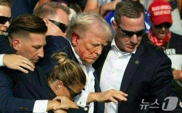 본문 이미지 - 도널드 트럼프 미국 공화당 대선 후보가 지난해 7월 펜실베이니아주 버틀러에서 열린 선거 집회서 유세를 하던 중 총격 사건이 발생해 얼굴에 핏자국을 묻은 가운데 경호원들과 긴급하게 대피를 하고 있다. 2024.07.14 ⓒ AFP=뉴스1 ⓒ News1 우동명 기자