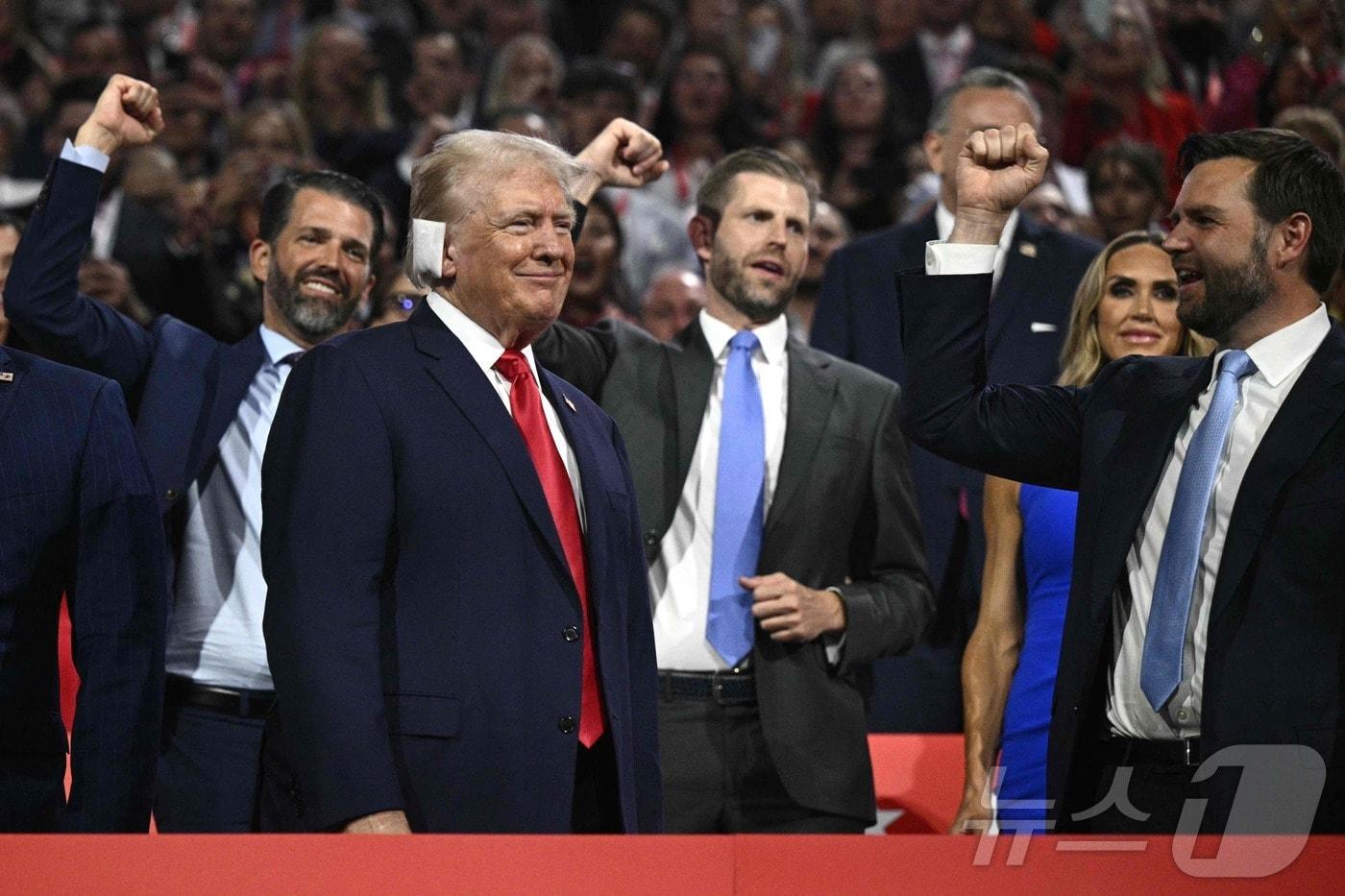 본문 이미지 - 15일(현지시간) 미 위스콘신주 밀워키 파이서브포럼에서 개막한 공화당 전당대회에 대선 후보인 도널드 트럼프 전 대통령이 귀에 붕대를 한 채 모습을 드러내자 그의 두 아들과 이날 부통령 러닝메이트로 지명된 제임스 데이비드 (J.D.) 밴스 상원의원(오하이오)이 주먹을 불끈 쥔 손을 치켜들고 그를 맞이하고 있다.  2024.07.16 ⓒ AFP=뉴스1