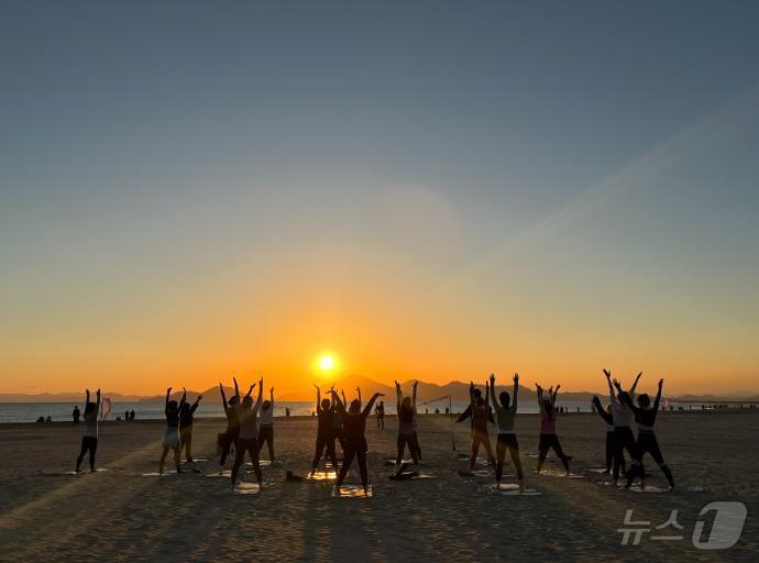 본문 이미지 - 해수욕장 백사장에서 해양치유프로그램 참가자들이 선셋필라테스를 하고 있다(부산시청 제공)